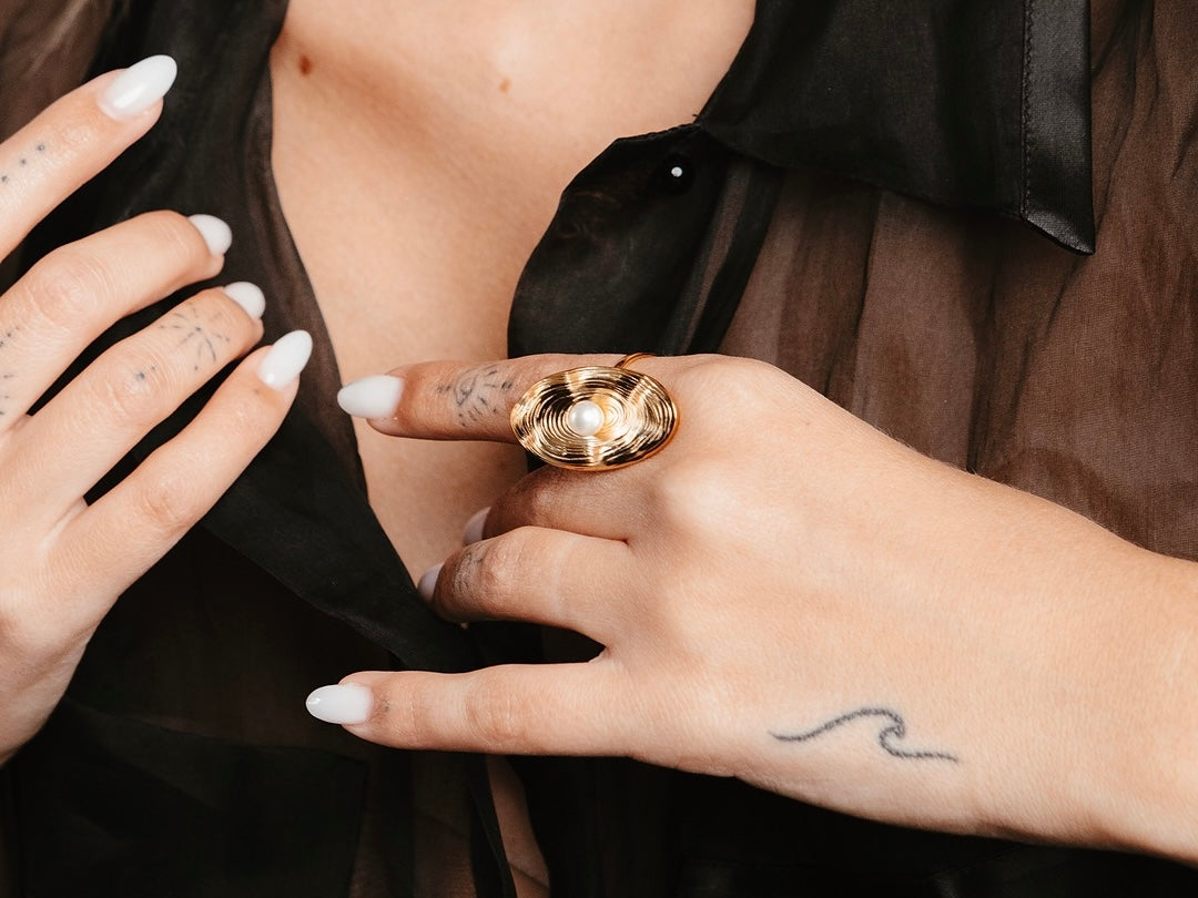 Mani di donna con smalto nero che indossano anelli dorati Medema lucidi e brillanti, guida alla cura dei gioielli placcati oro