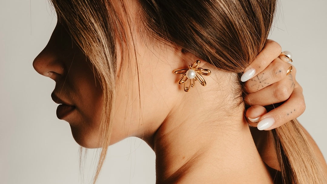 Donna con capelli raccolti che tocca delicatamente orecchini dorati Medema eleganti, guida come scegliere gioielli per ogni occasione