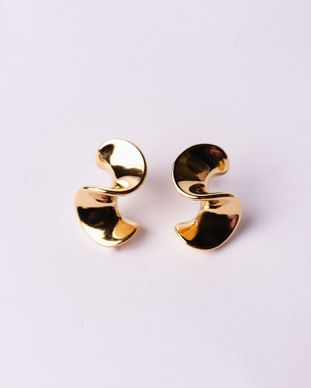 Dettaglio orecchini dorati Medema con superficie lucida e avvolgente