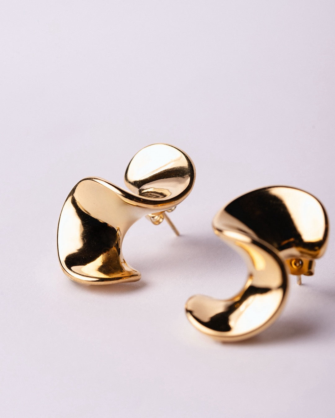 Orecchini Cairo Fluidi su sfondo bianco, linee organiche e luce dorata