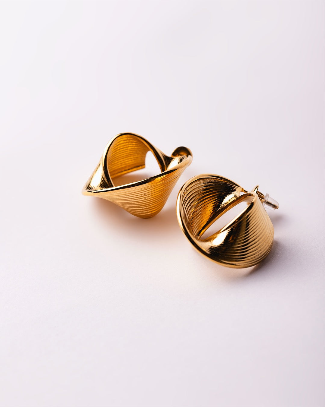 Dettaglio orecchini dorati Medema con texture ondulata e finitura lucida