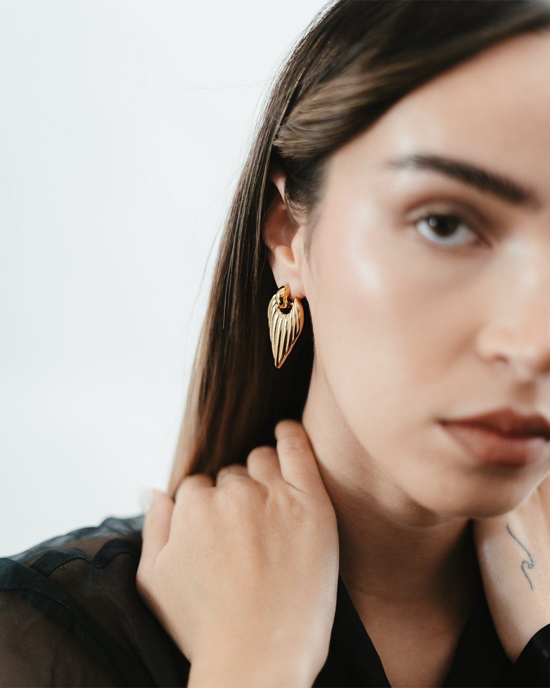 Primo piano del viso con Orecchini Medema Roma Scultorei, design verticale e lucentezza dorata