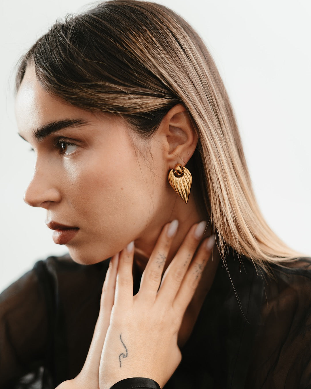 Vista laterale della modella con Orecchini dorati Medema, forma allungata e scultorea