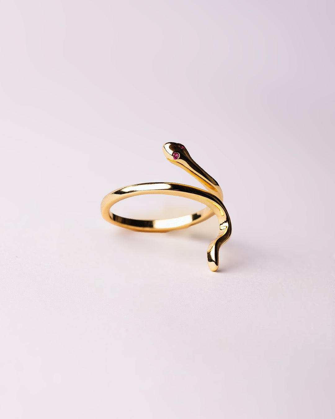 Dettaglio anello dorato a forma di serpente con piccole pietre verdi sugli occhi