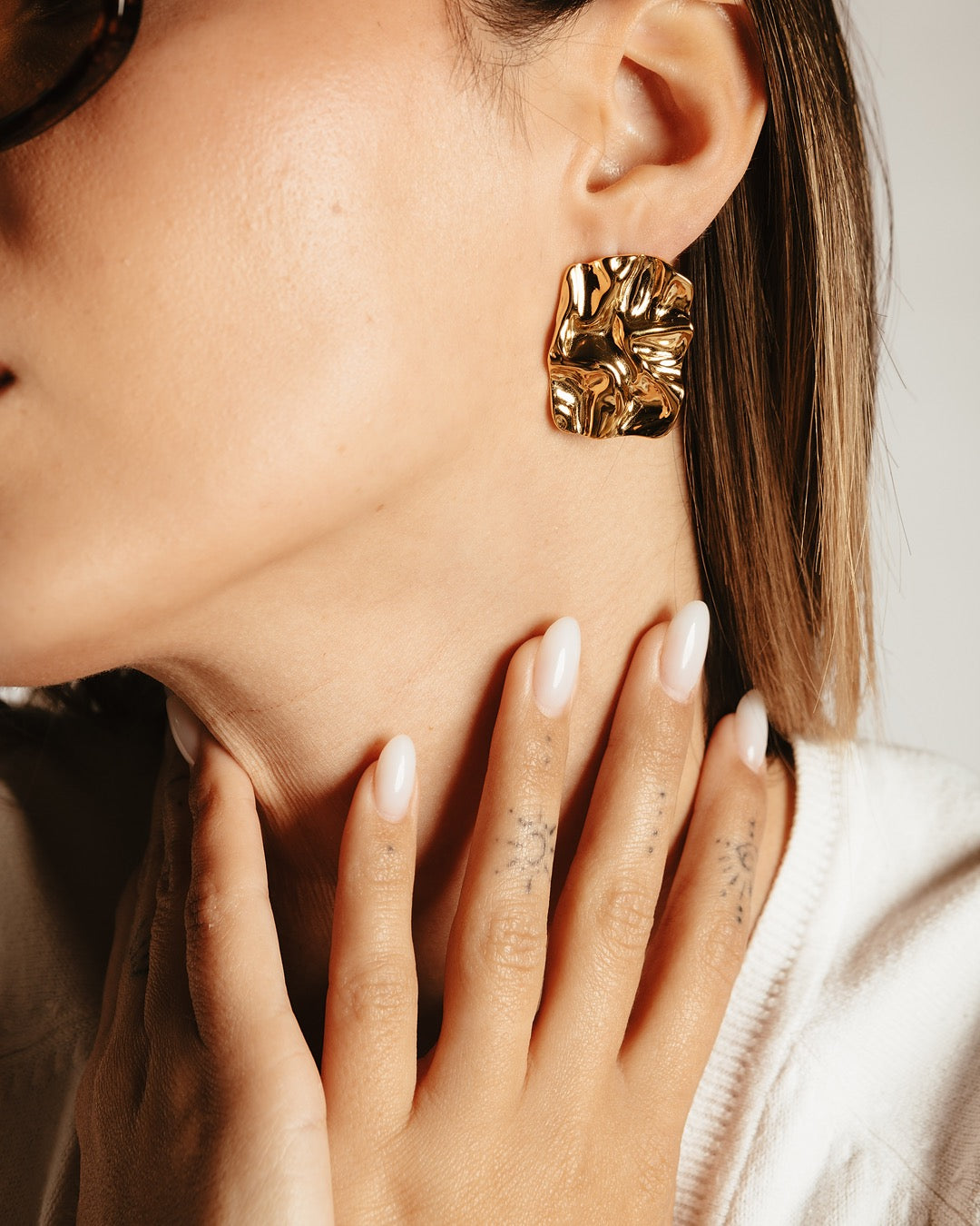 Dettaglio del viso con orecchini dorati Medema, superficie irregolare e luminosità dorata