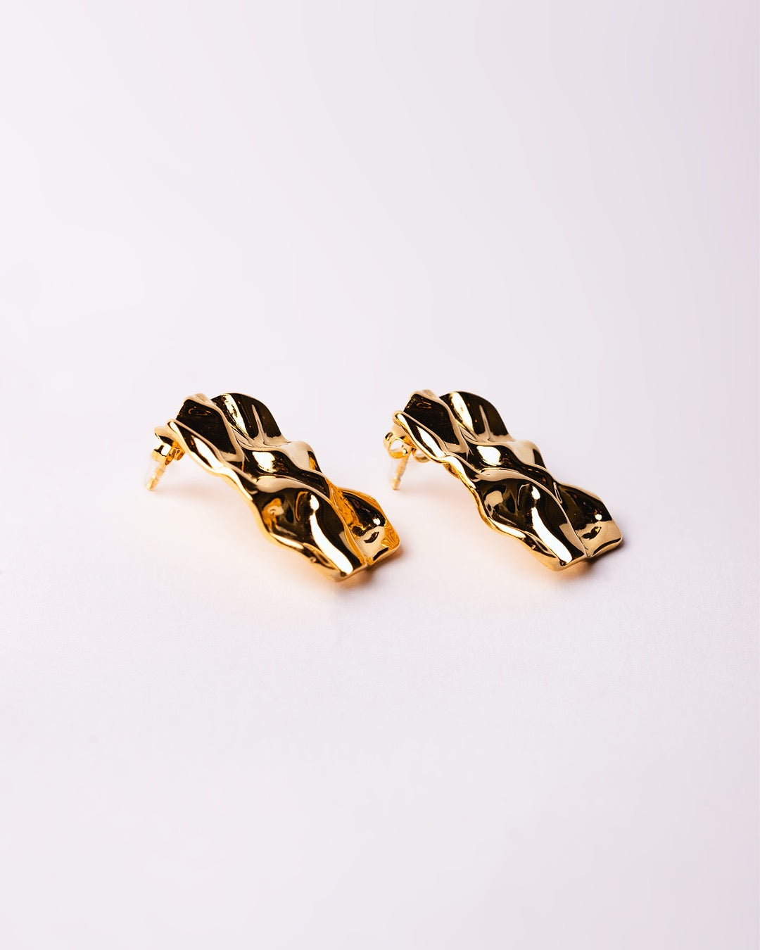 Vista laterale degli orecchini dorati Medema, finitura lucida e dinamica effetto scultura