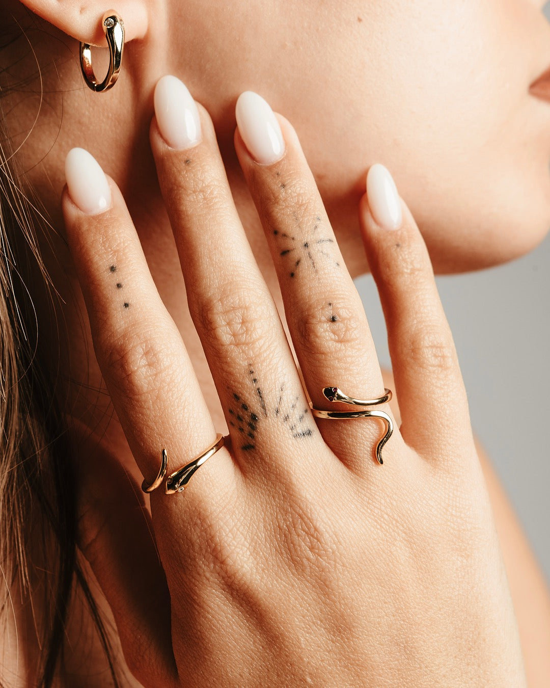 Dettaglio laterale degli orecchini dorati Bangkok e anelli serpente indossati, con luce che illumina il volto