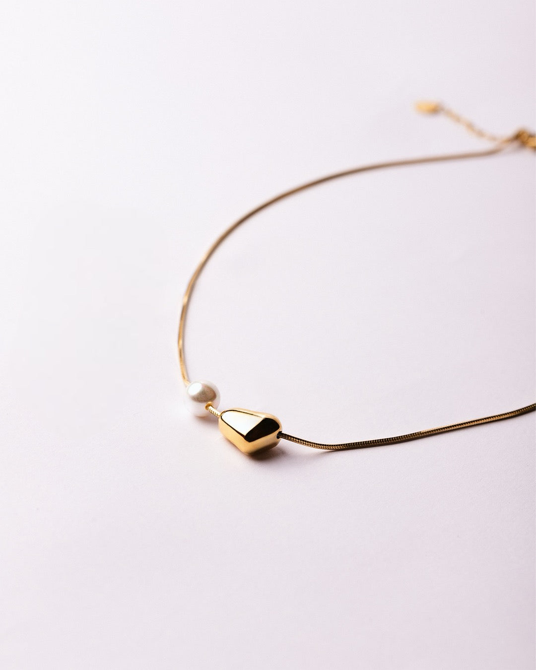 Collana Medema Atene su sfondo chiaro, perla sferica e forma scultorea in armonia