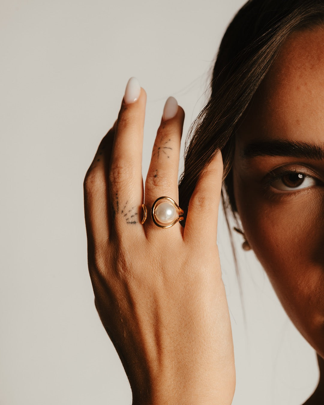 Dettaglio della mano con Anello Medema Atene Spirale di Luce, luce dorata e perla centrale