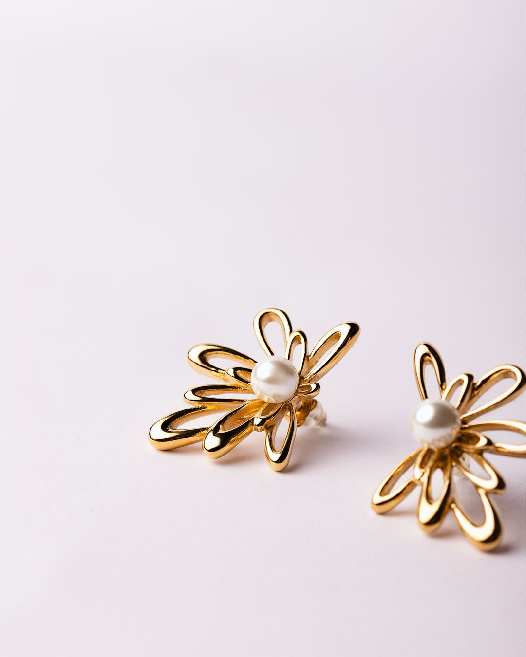 Orecchini Atene Fiore Dorato Medema su sfondo chiaro, petali intrecciati e luce naturale