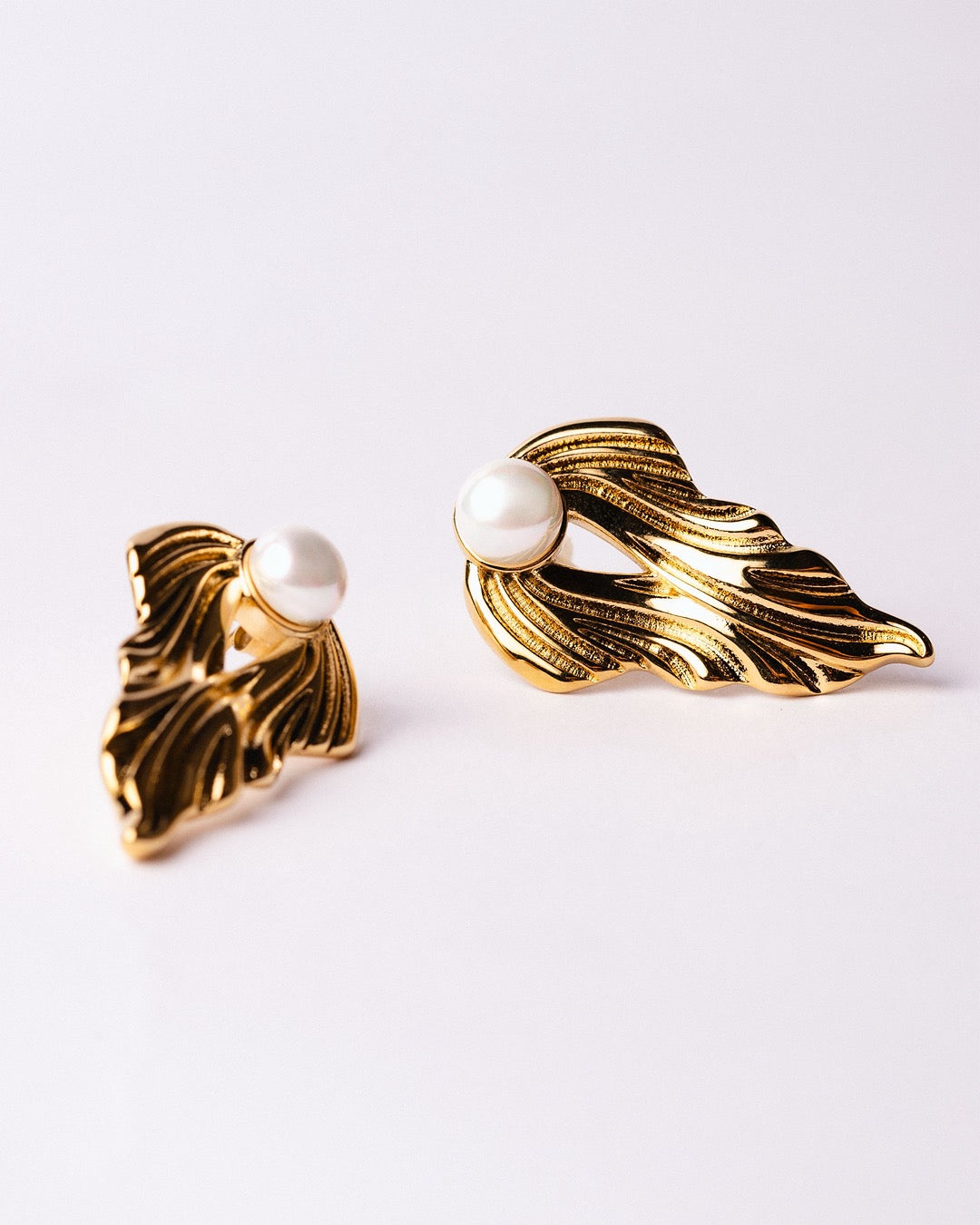 Orecchini Medema Atene Onde Dorate su sfondo chiaro, finitura a specchio e perla centrale